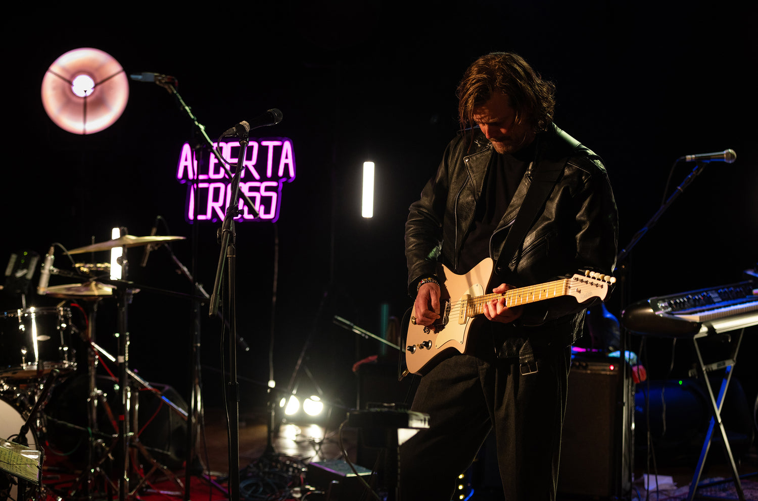 Petter Erikson playing pink West Valley guitar on stage with 'Alberta Truss' sign in the background

