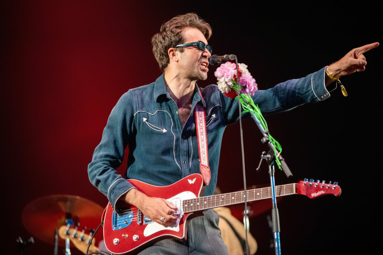 Person playing guitar and pointing, with a microphone and flowers on stage
Justin Hayward-Young from the Vaccines
